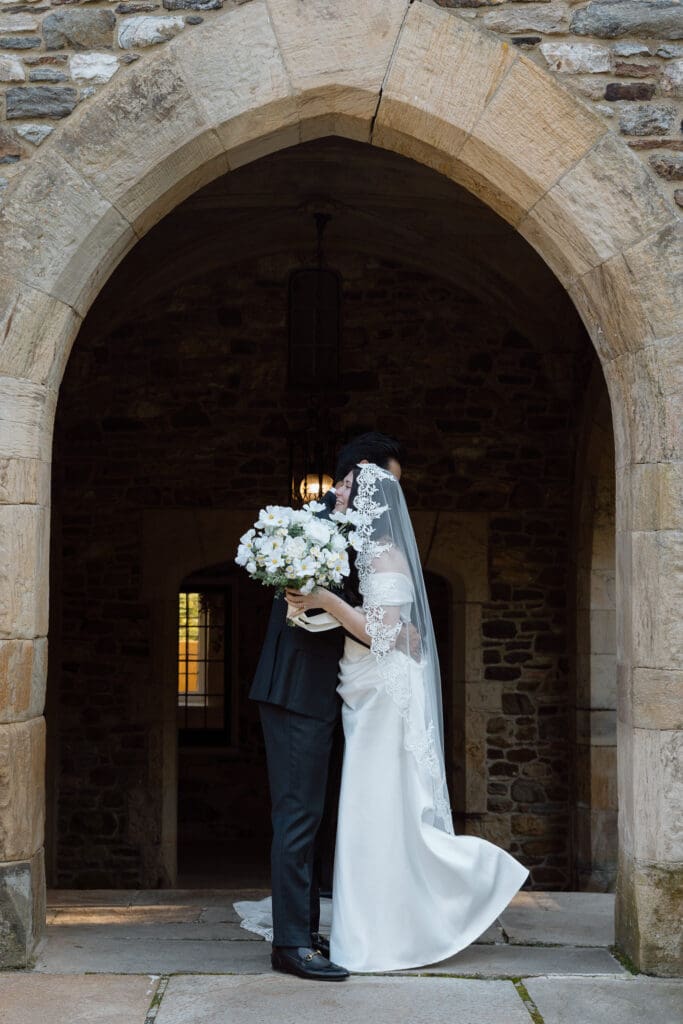 Bride and groom hugging beneath a stone arch at Parque at Ridley Creek
